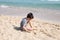 Kid playing with sand on the beach alone. Little boy near sea. Summer play