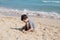 Kid playing with sand on the beach alone. Little boy near sea. Summer play