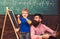 Kid reciting a poem while teacher listens attentively. Cool guy in pink shirt sitting on floor next to standing kid