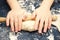 Kid`s hands, some flour, wheat dough and rolling-pin on the black table. Children hands making the rye dough for backing bread. S