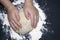 A kid`s hands, some flour, wheat dough and rolling pin on the black table with a place for text. Children hands making the rye do