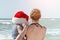 Kid in Santa hat in the arms of mother, the beach. Back view