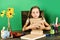Kid and school supplies, green background. Girl with bored face
