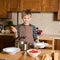 Kid serving Borshch, traditional Russian and Ukrainian soup. Pouring soup into a plate with ladle from pan in kitchen.