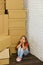 Kid sits on floor in corner. Child among cardboard boxes