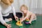 The kid sits on the rug, plays with his mother, collects a pyramid.