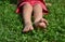 Kid sitting bare footed on the green grass, clover leaves, in red shorts. Child`s feet on the grass, toes, happy feeling, warm