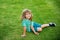 Kid sitting on grass field. Cute boy run in summer park. Child running on meadow.