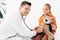 Kid and smiling pediatrist in white coat examining teddy bear with stethoscope