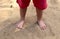 Kid standing bare footed on the sand in red shorts. Child`s feet with cute toes, happy feeling, warm sumer day, Earth day