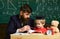 Kid studies individually with teacher, at home. Teacher and pupil in mortarboard, chalkboard on background. Father with