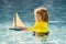 Kid with toy boat in sea water on summer vacation. Little boy playing with toy seailing boat on sea. Summer vacation