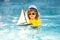 Kid with toy boat in sea water on summer vacation. Little kid playing with toy seailing boat on sea. Summer vacation