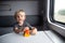 Kid in a train compartment looks out the window. The passenger with a toy travels in the train cabin