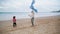 Kid trying launching kite with mom on windy beach. Excited mother helping son