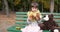 Kid with two pieces of bun with poppy in hands sits near teddy bear on bench at playground in autumn park