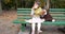 Kid with two pieces of sweet bun in hands sits on bench with toy at playground in autumn park