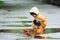 Kid in yellow waterproof cloak and boots playing with paper handmade boat toy outdoors after the rain