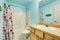 Kids bathroom in blue tones with wooden cabinets and colorful shower curtain.