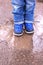 Kids boots in muddy puddle. Colorful winter outdoor rain shoes on childrens feet in action. A child on stay in the mud