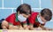 Kids busy in writing with medical face mask wearing due to covid-19 or coronavirus outbreak or pandemic at school -