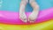 Kids feet laying relaxing on colorful rainbow inflatable swimming pool. Young girl in pink swimsuit playing in water 4K