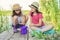 Kids girls sitting on wooden pier, catching water snails in bucket