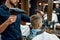 Kids haircut. Young Barber drying hair of little boy sitting in barber shop chair in front of the mirror. Barbershop