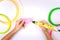 Kids hand holding yellow 3d pen with colorful filaments and makes heart on white background