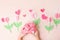 Kids hands holding gift present box with pink bow decorated paper hearts and tulip flowers on pink pastel table top view. Flat lay