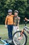 Kids in helmets embracing and looking at camera while standing near bicycles at park