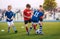 Kids Kicking Football Ball. Boys Play Soccer on Grass Field. Spectators Parents in the Background