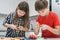 Kids play toy constructor standing above kitchen table and looking down. Boy and girl collect colored details of lego.