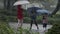 Kids in the pouring rain having fun jumping with umbrellas - slow motion