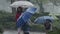 Kids in the pouring rain having fun jumping with umbrellas - slow motion