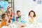 Kids sitting at table with cake and blowing party horns during birthday celebration.