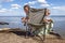 Kids sitting on touristic armchair, eating croissants and looking at sea during vacation at campsite