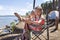 Kids sitting on touristic armchair, eating croissants and looking at sea during vacation at campsite