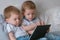 Kids with tablet. Two boys twins toddlers looking cartoon at tablet lying on the bed.