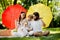 Kids and their parents sitting on the blanket under the big red and yellow umbrellas covering them from the sun.