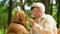 Kind man with visual impairment petting guide dog, sitting on bench in park