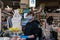 Kindly young man cashier working at supermarket wearing face mask and gloves. People buying food at SuperFresh due to the Covid19