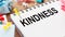 KINDNESS - text on a notepad with wrinkled paper and paper needles on wooden background