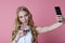 Kinky blonde girl shoots herself smartphone smiling on pink Studio background