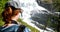 Kinsarvik, Hordaland, Norway. Young Woman Lady Tourist Traveler Taking Pictures Of Waterfall Nyastolfossen In