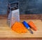 Kitchen grater, grated and uncleaned whole carrots on cutting board