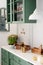 Kitchen with green vintage furniture, pendant lights, marble counter top with flowers and pumpkins, pots of autumn flowers,