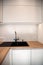 Kitchen interior. A black washbasin, tall brass faucet in a white kitchen with a wooden countertop