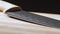 Kitchen knife laying on wooden desk, close shot. Camera moving from knifepoint to handle. Carvings on dark blade