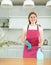 in kitchen,positive woman hostess in dotted red apron stands and holds rag and cleaning spray